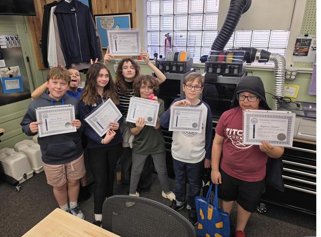 Young people holding certificates in the makerspace.